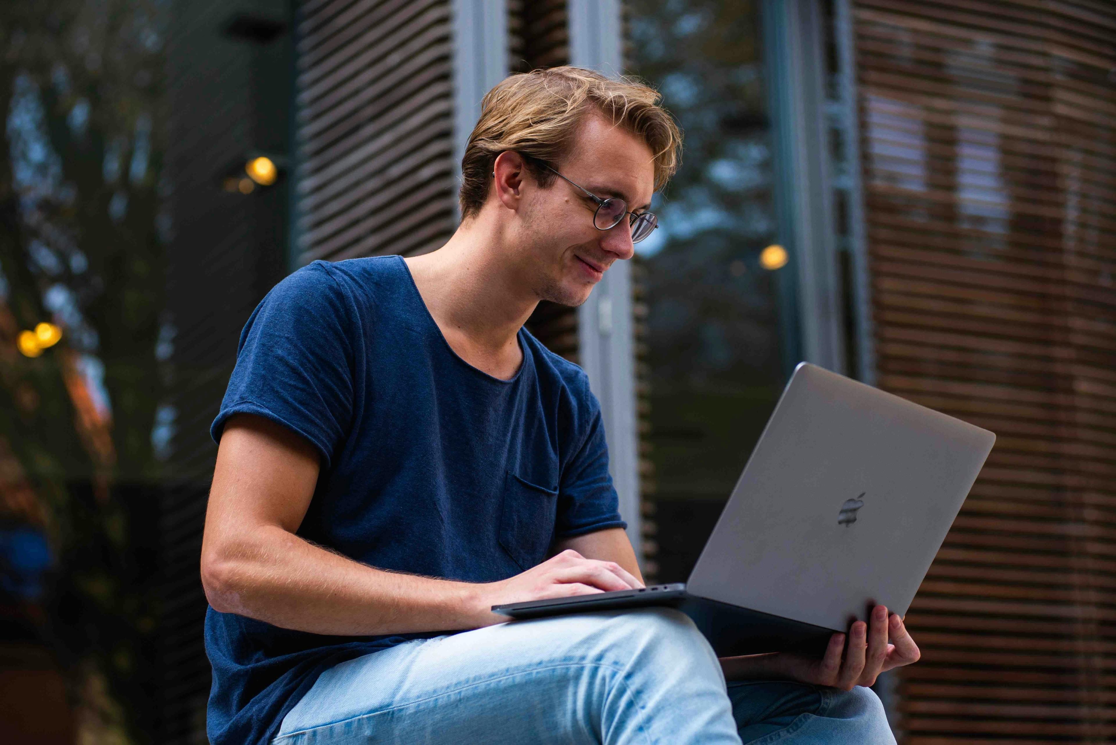 Man zittend glimlachend kijkend naar laptop op zijn schoot buiten