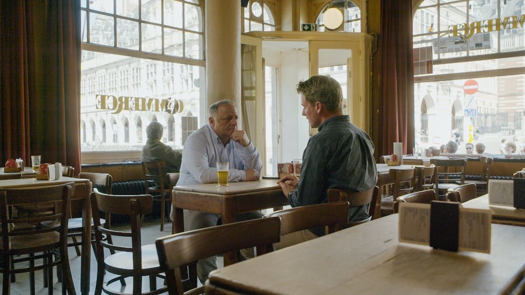 Sander Schimmelpanninick zittend aan houten tafel met Marc van Ranst bij een bar